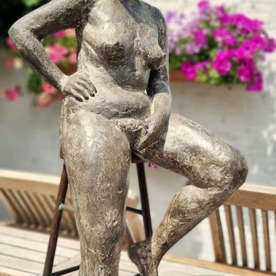 Bronze sculpture of a seated female nude on a stool.